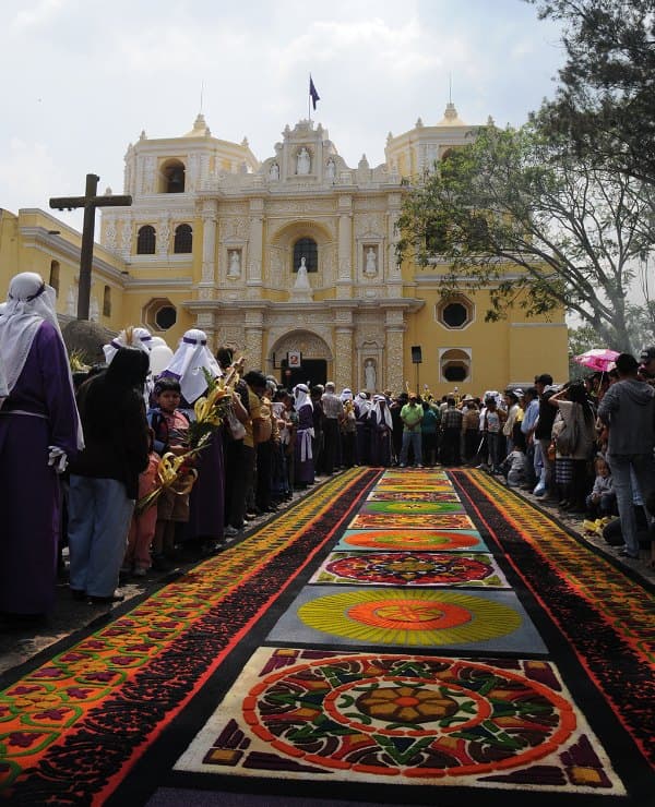 A Holy Week carpet of colored sawdust laid on the street in front of the yellow church of La Merced in Antigua Guatemala, with a crowd on both sides